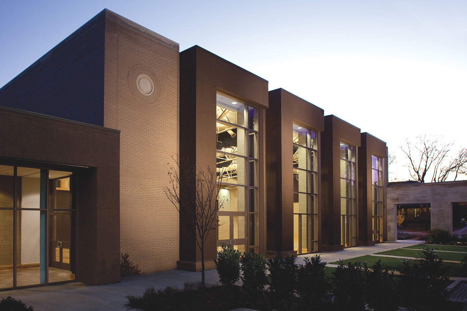 The Belmont United Methodist Church community center at dusk, tall glazed bays lit from within between brick piers.